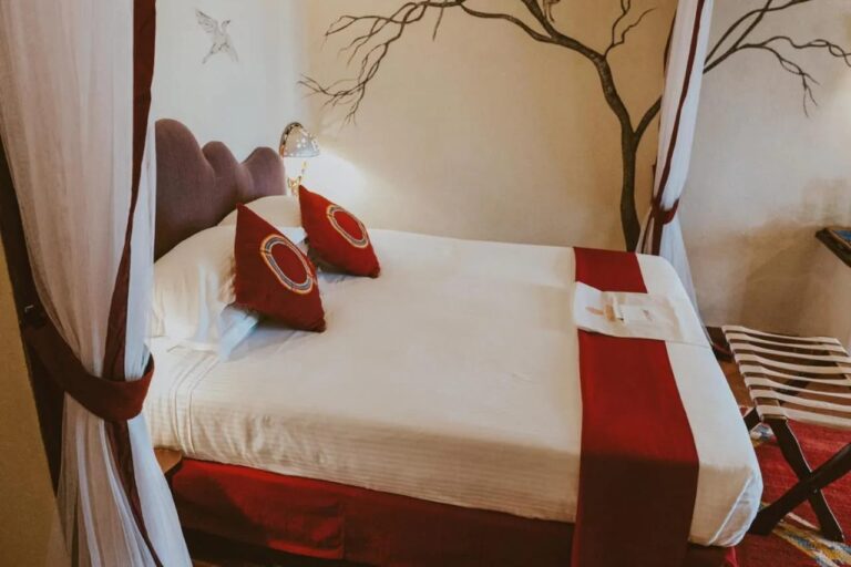 Un grande letto con cuscini rossi tra due tende bianche, davanti a un albero dipinto sul muro