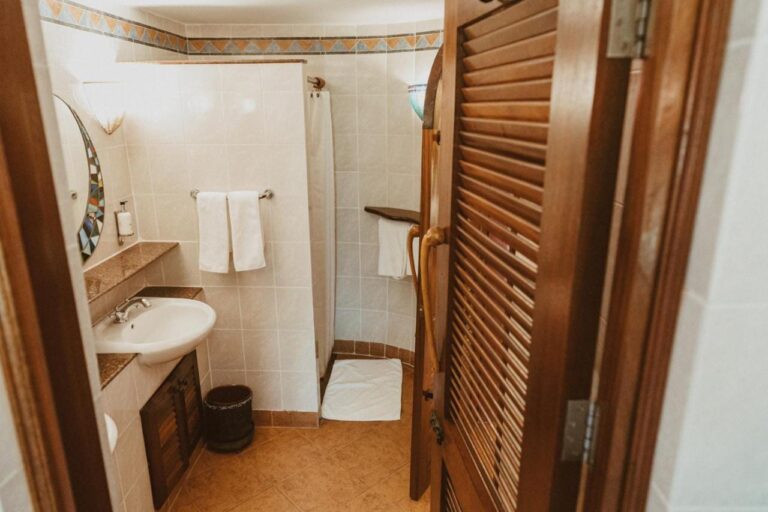 Un bagno visto dalla porta in legno a persiana, con un lavabo e una doccia con tenda