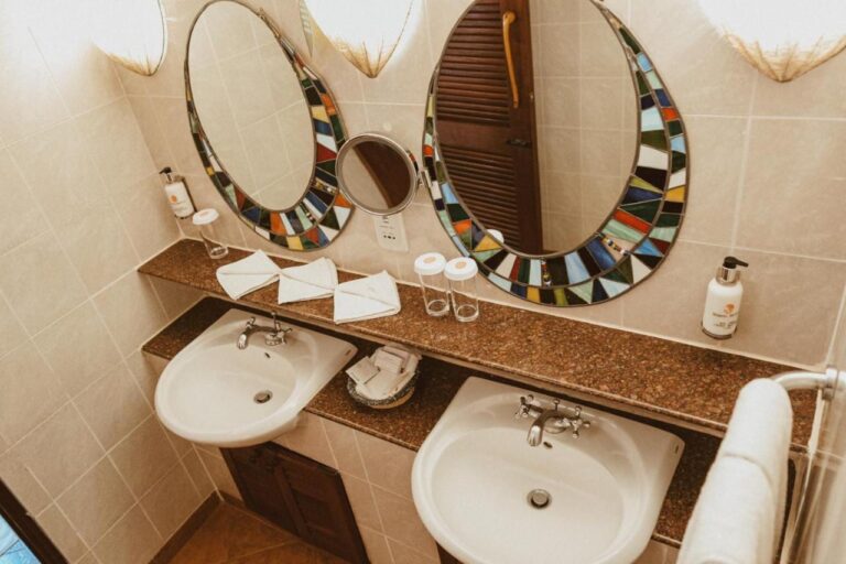 Un bagno con due lavabi e uno specchio ingranditore tra due specchi a mosaico