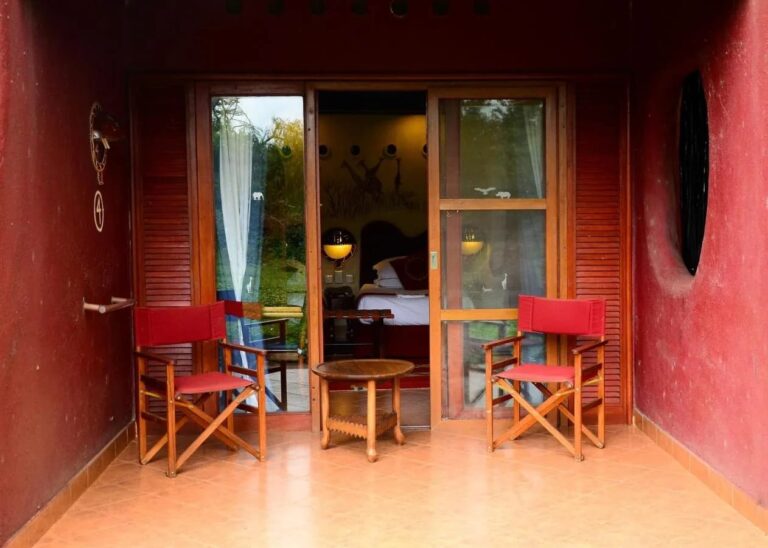 La terrazza di una camera tra due muri rossi, con due sedie pieghevoli rosse e un tavolino rotondo