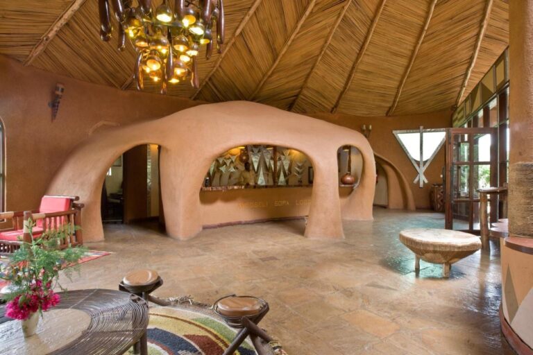 La hall con i muri di terra scolpiti ad archi, sotto un soffitto di canne e un lampadario