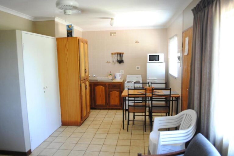 La zona giorno di uno chalet, con angolo cottura, tavolo da pranzo, armadio in legno e una sedia bianca