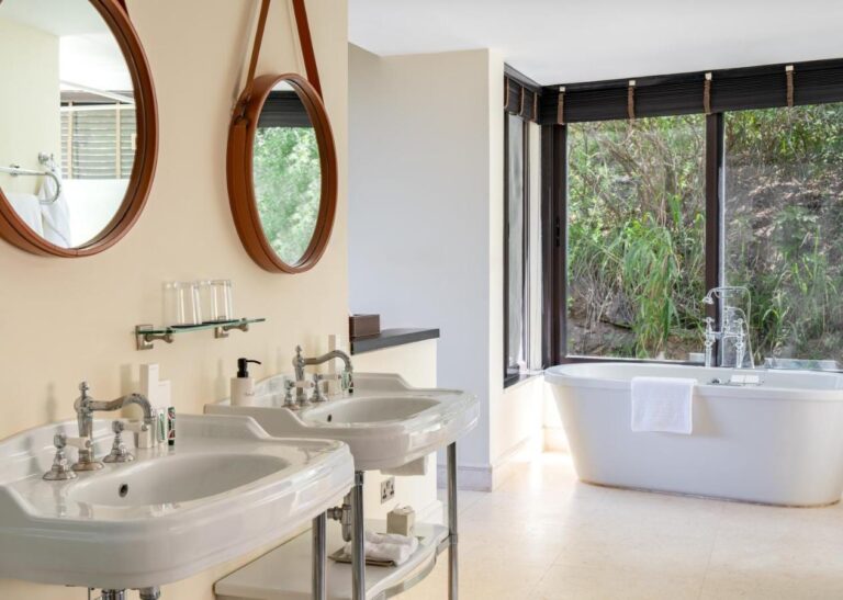 Un bagno con due lavabi a colonna, specchi rotondi e una vasca davanti a una grande vetrata