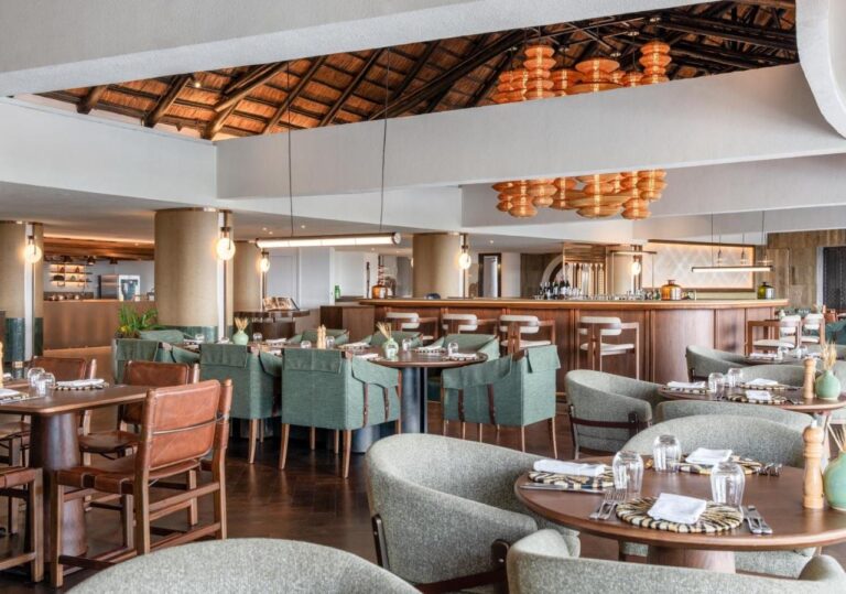 Un ristorante con poltroncine verdi, davanti a un lungo bancone, sotto lampade a sospensione arancioni