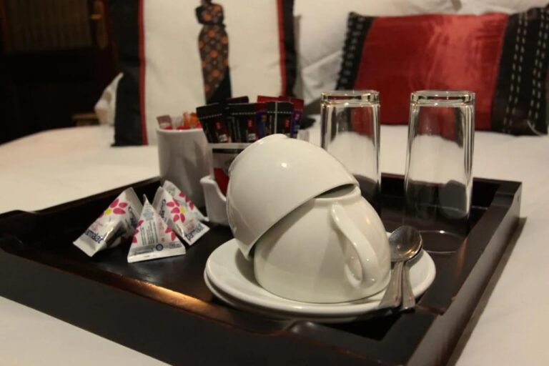 Un vassoio con tazze, bicchieri e bustine di tè e caffè, appoggiato su un letto
