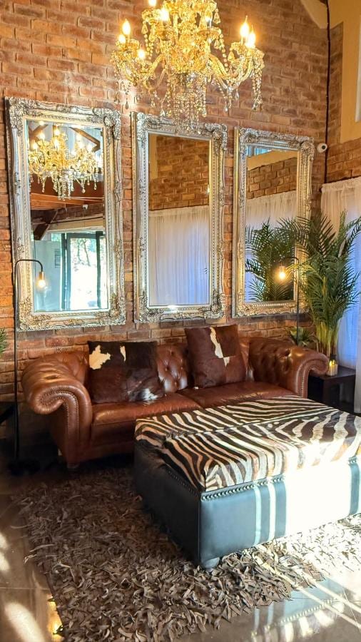 Un divano Chesterfield in pelle e un pouf zebrato sotto un lampadario di cristallo, davanti a tre grandi specchi e a un muro di mattoni