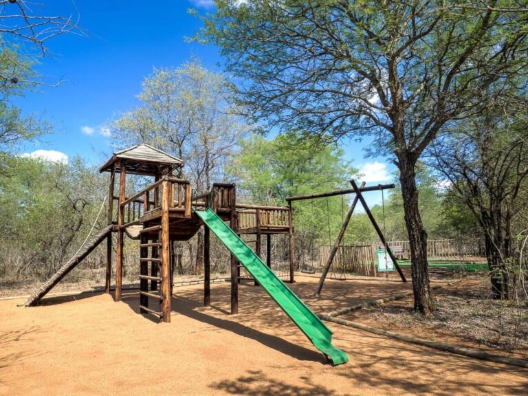 Il parco giochi per bambini, con una torre in legno, uno scivolo verde e un'altalena, sotto gli alberi