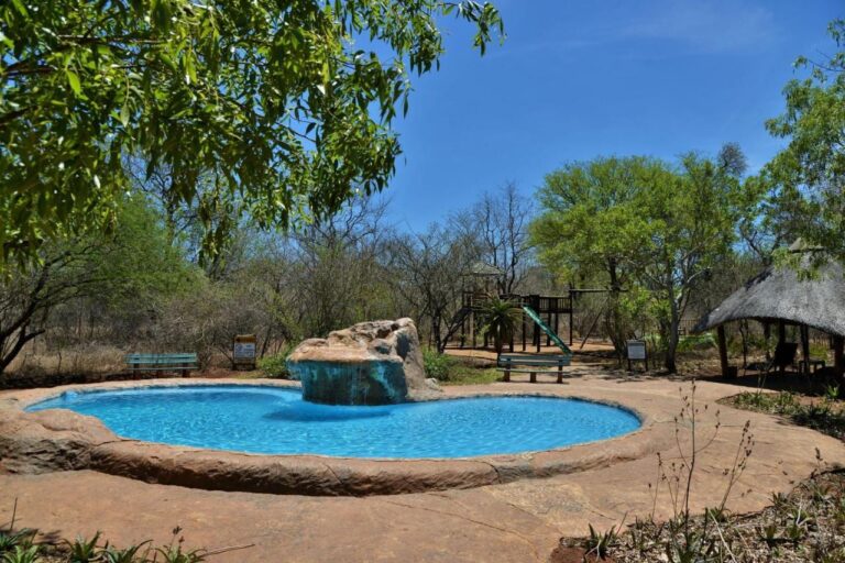 La piscina con cascata del Jackalberry Ridge sotto un cielo azzurro, circondata da panchine e alberi