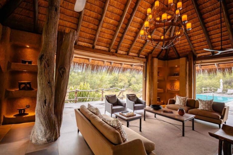 Il salone del Kapama River Lodge sotto un alto tetto di paglia, aperto su una piscina e sulla boscaglia