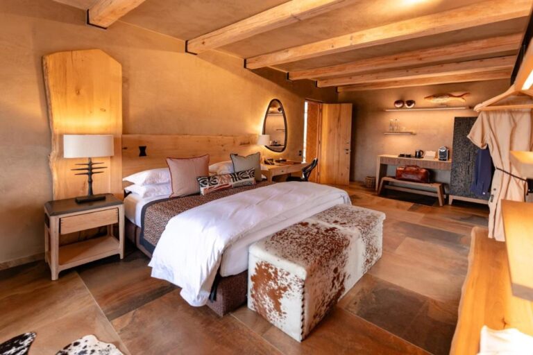 Una suite con un grande letto, una panca in pelle di mucca, un angolo caffè e un accappatoio appeso