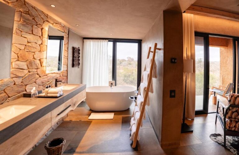 Il bagno di una suite, con una vasca davanti alla finestra e un doppio lavabo contro un muro di pietra