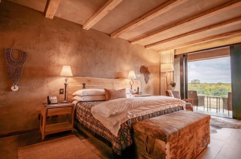 Una suite con un grande letto, una carta dell'Africa in legno al muro e una terrazza sulla boscaglia