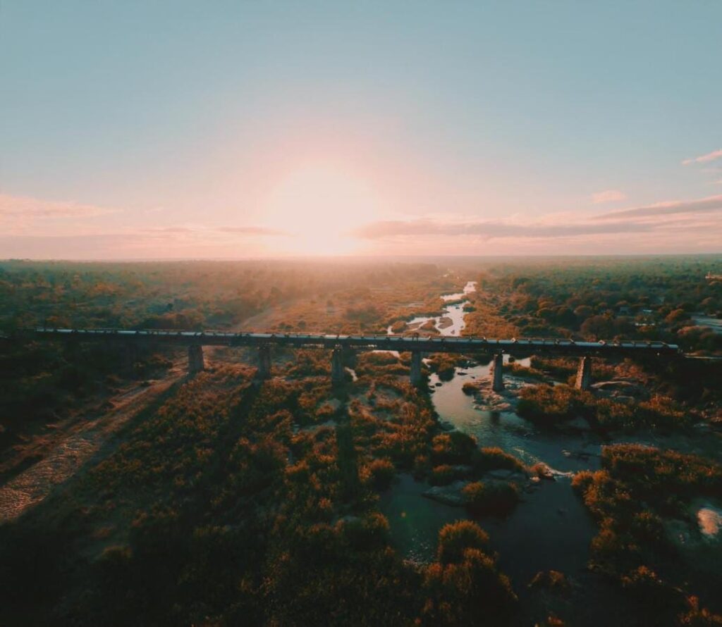 Il treno del Kruger Shalati sul ponte Selati, visto dall'alto, sopra il fiume e la boscaglia, con il sole basso sull'orizzonte