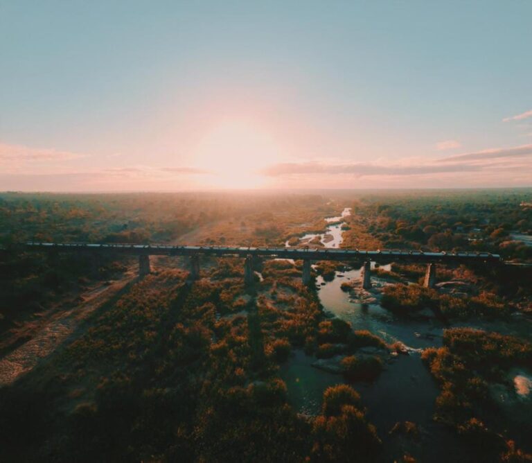 Il treno del Kruger Shalati sul ponte Selati, visto dall'alto, sopra il fiume e la boscaglia, con il sole basso sull'orizzonte