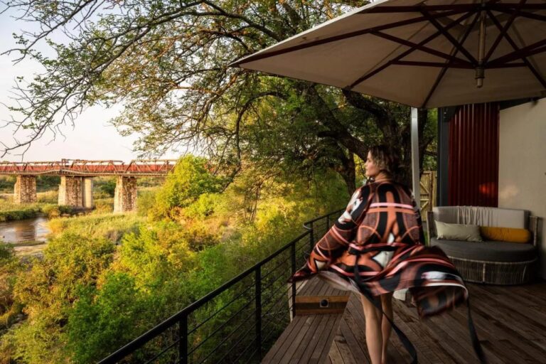 Una donna in accappatoio su una terrazza in legno, sotto un ombrellone, davanti al ponte e al fiume