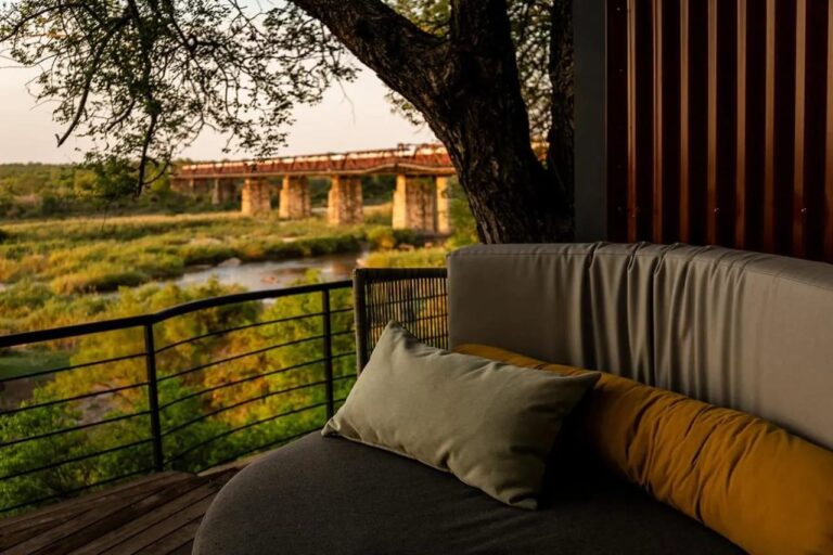 Un divanetto curvo su una terrazza, sotto un grande albero, davanti al ponte e al fiume