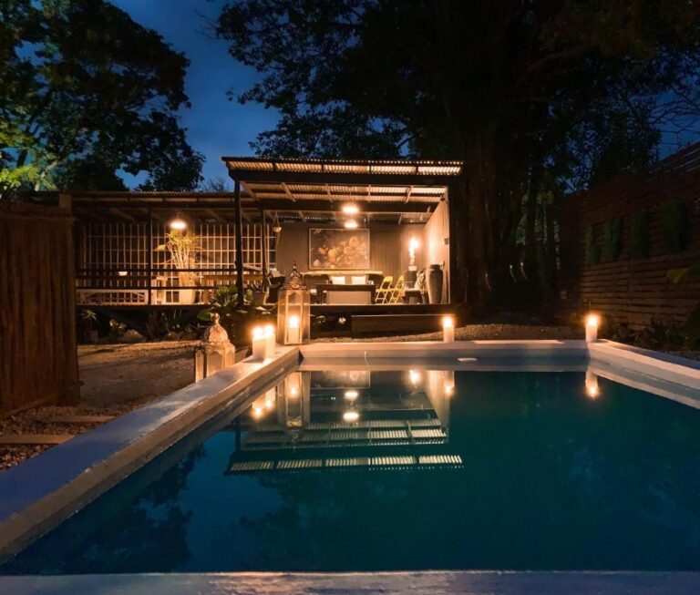 La piscina del Lush al calar della sera, illuminata da candele, davanti a una terrazza coperta con il tetto in lamiera