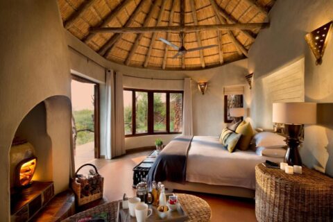 Una suite del Madikwe Safari Lodge sotto un tetto di paglia, con un grande letto e un camino acceso