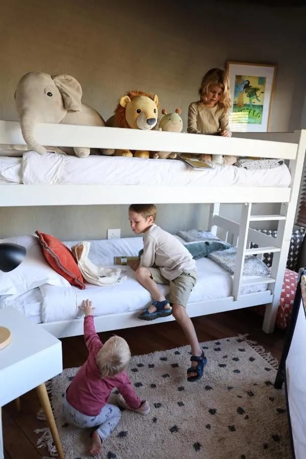 Tre bambini giocano intorno a un letto a castello, con peluche di elefante e di leone