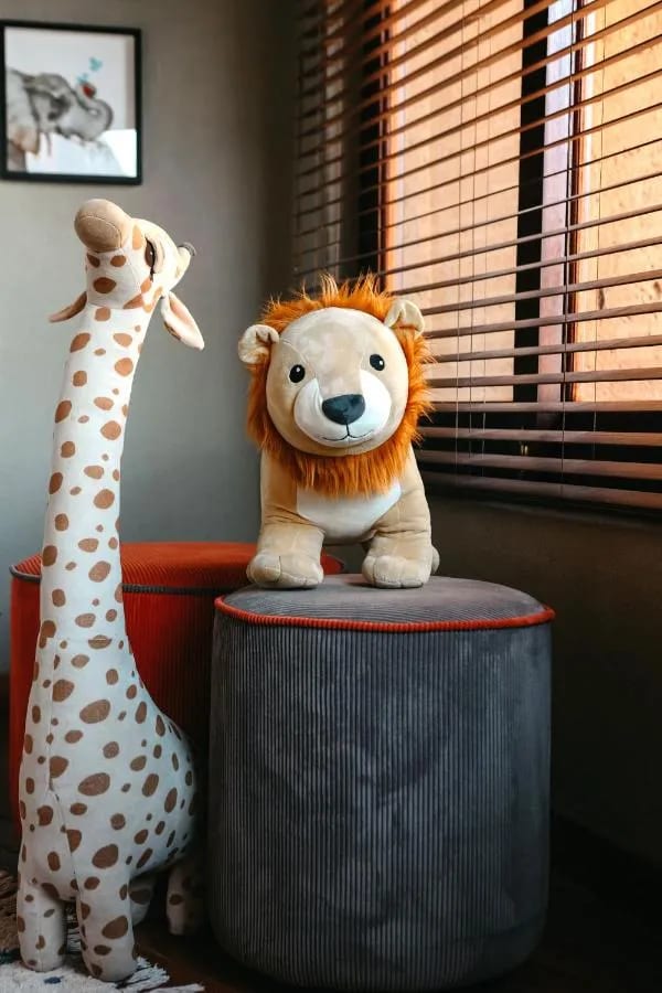 Una giraffa e un leone di peluche vicino a una finestra con le tende a rullo