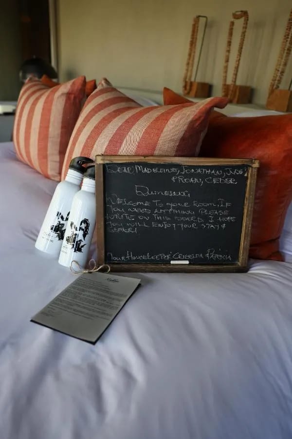 Un messaggio di benvenuto scritto col gesso su una lavagnetta, appoggiata sul letto con due borracce