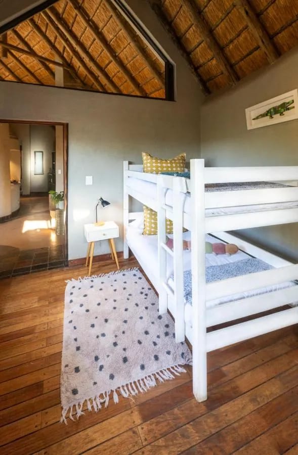Un letto a castello bianco sotto la travatura di paglia, su un parquet con un tappeto a pois