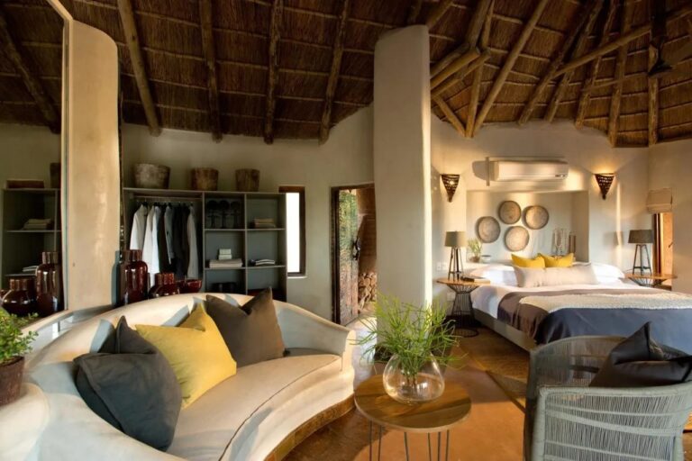 Una suite del Madikwe Safari Lodge con un divano bianco curvo, un grande letto e un guardaroba aperto