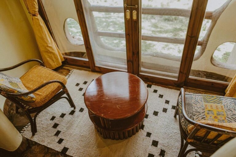 Due poltrone e un tavolino rotondo davanti a una porta-finestra, con la savana oltre la balaustra del balcone