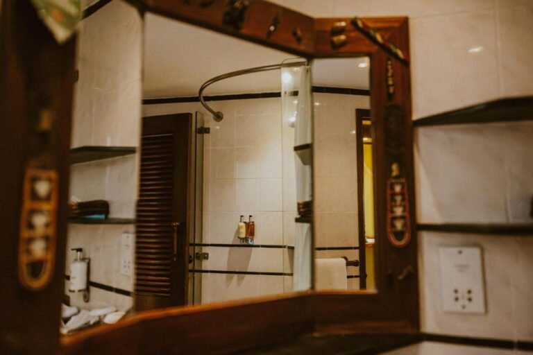 La doccia in vetro di un bagno, vista in uno specchio con la cornice di legno intagliato