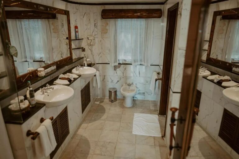 Un bagno in marmo bianco, con due lavabi, un asciugacapelli a parete e un bidet sotto la finestra