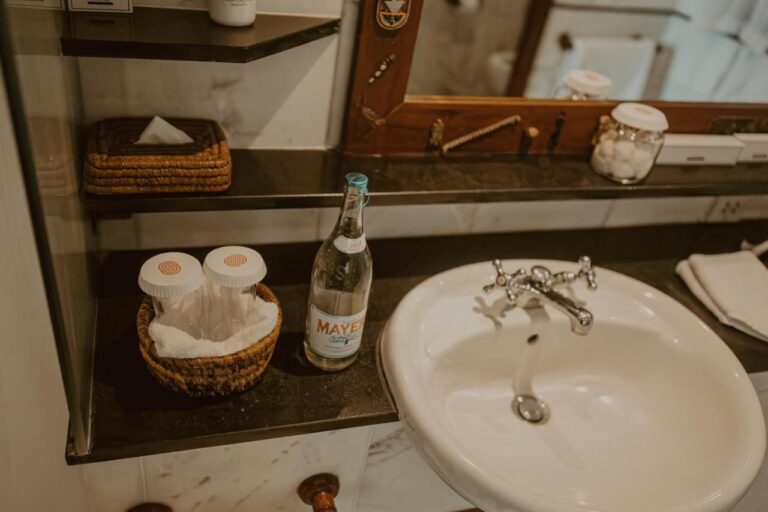Un lavabo con una bottiglia d'acqua, dei dischetti di cotone e una scatola di fazzoletti in vimini