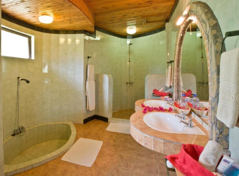 Un bagno piastrellato di verde, con un piatto doccia rotondo incassato e due lavabi sotto uno specchio ad arco