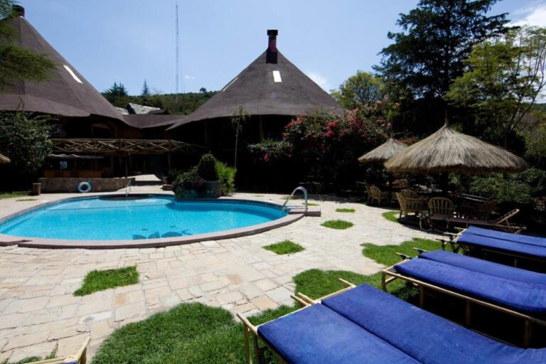 Sdraio con cuscini blu a bordo piscina, vicino a ombrelloni di paglia