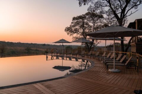 La piscina a sfioro del Mdluli Safari Lodge sotto un cielo arancione, circondata da sdraio e ombrelloni