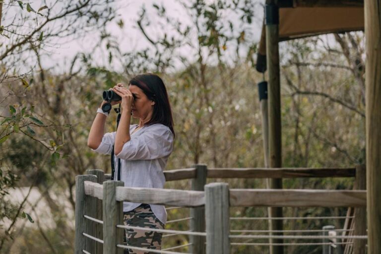 Una donna con il binocolo sulla terrazza in legno di una tenda, davanti alla boscaglia