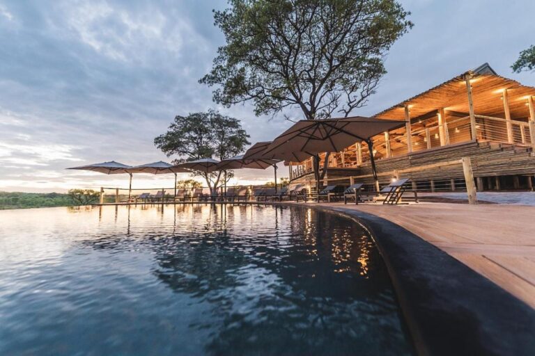 La piscina a sfioro del Mdluli Safari Lodge e il suo edificio principale illuminato, sotto un cielo nuvoloso