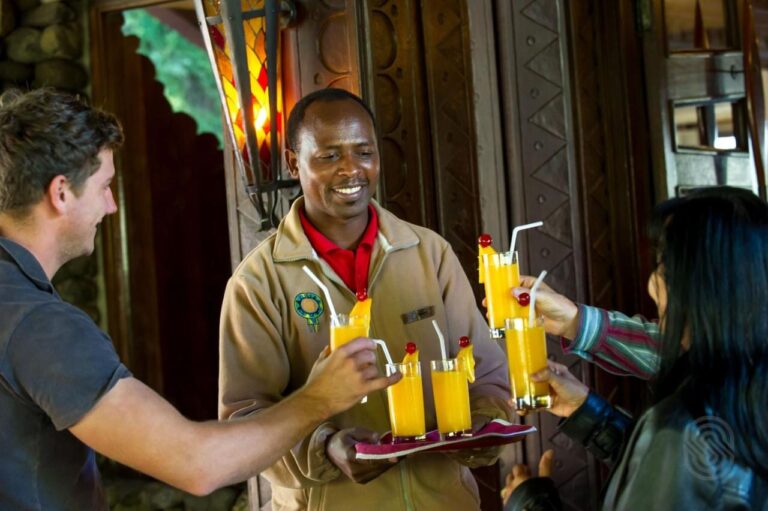 Un membro del personale del Ngorongoro Serena Safari Lodge porge un vassoio di succhi di frutta a due viaggiatori