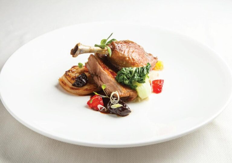 Una coscia di pollame arrosto con le sue verdure su un piatto bianco
