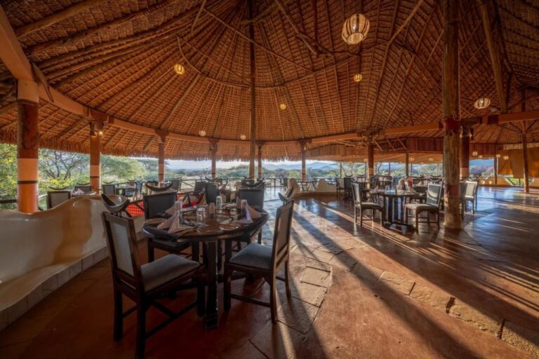 La sala del ristorante sotto un immenso tetto di paglia, aperta sulle acacie e sulle colline