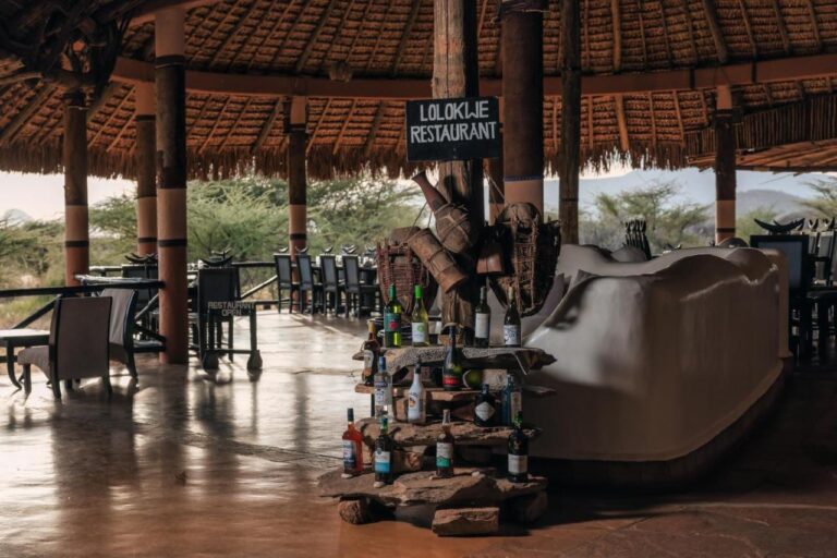 L'ingresso del ristorante Lolokwe, con bottiglie di vino appoggiate sulle pietre, sotto un grande tetto di paglia