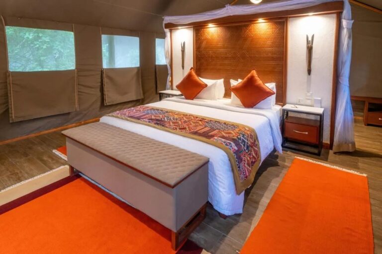 Il letto di una tenda visto di lato, con la testiera in legno e i tappeti arancioni