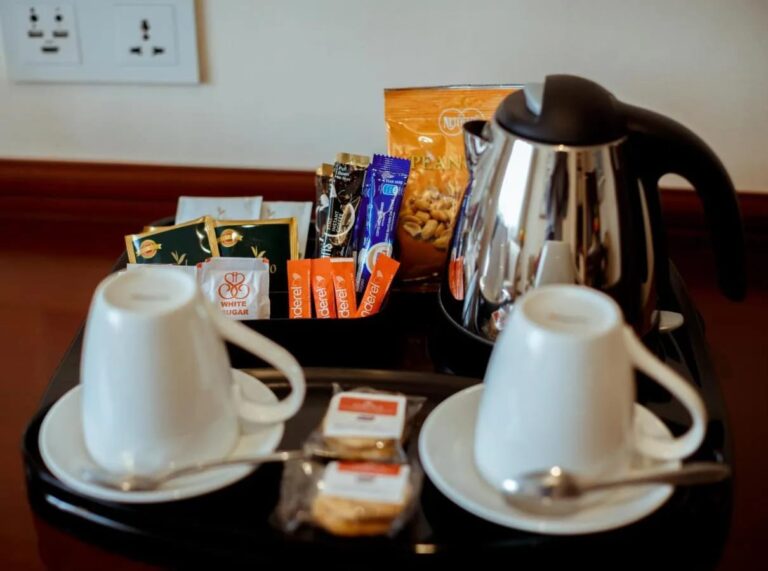 Un vassoio con bollitore, due tazze, tè, caffè in bustine e biscotti
