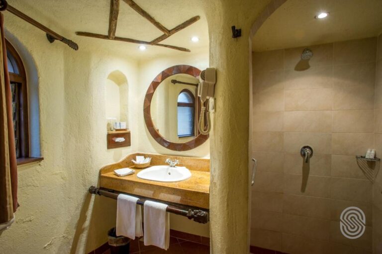 Un bagno con le pareti intonacate, un lavabo sotto uno specchio rotondo e una grande doccia piastrellata