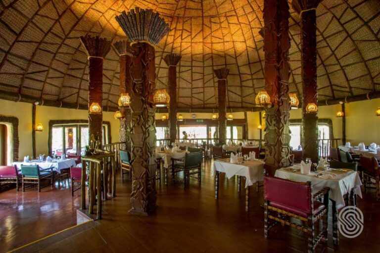 La sala del ristorante sotto la cupola, con le colonne di legno scolpite con figure umane e i tavoli dalle tovaglie bianche