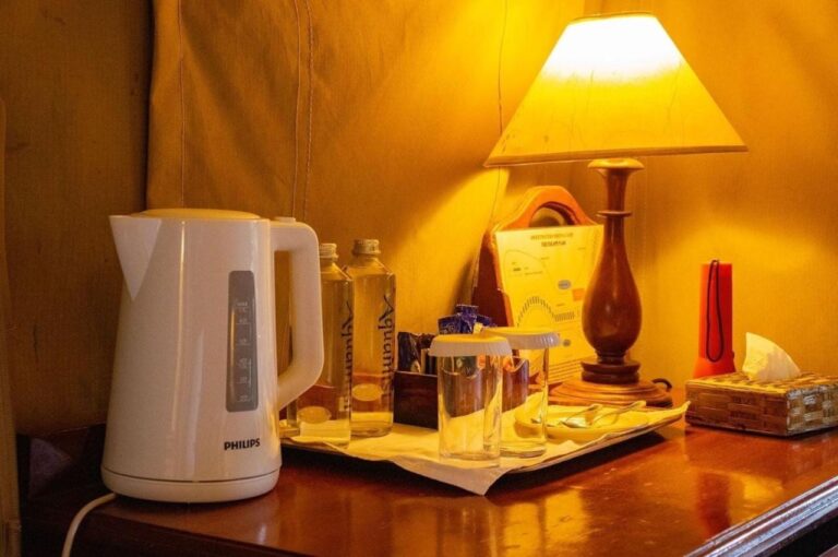 Un bollitore, bottiglie d'acqua e bicchieri su una scrivania, sotto una lampada