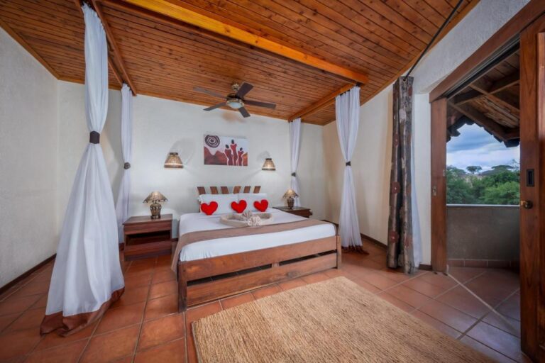 Una camera con un grande letto sotto un soffitto in legno, con tende velate e un balcone
