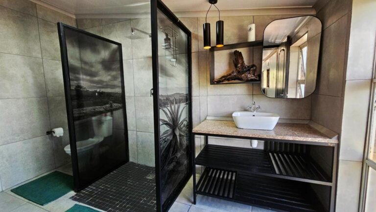Un bagno con una doccia dietro pareti di vetro decorate con foto in bianco e nero, e un lavabo d'appoggio su un mobile nero