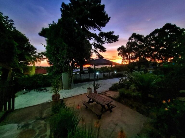 Il giardino al tramonto, con un tavolo da picnic sotto grandi alberi e un cielo arancione