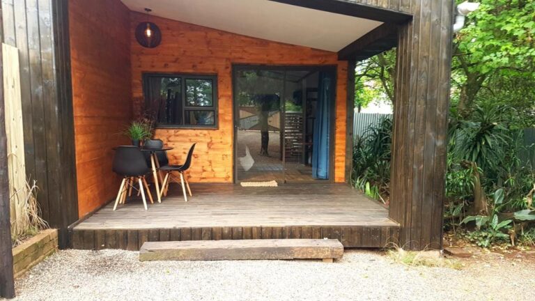 La terrazza in legno di uno chalet, con un tavolo e due sedie nere davanti a una porta a vetri scorrevole
