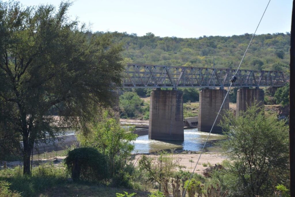 Un ponte metallico su piloni di cemento sopra l'Olifants, visto dal giardino del Three Bridges B&B